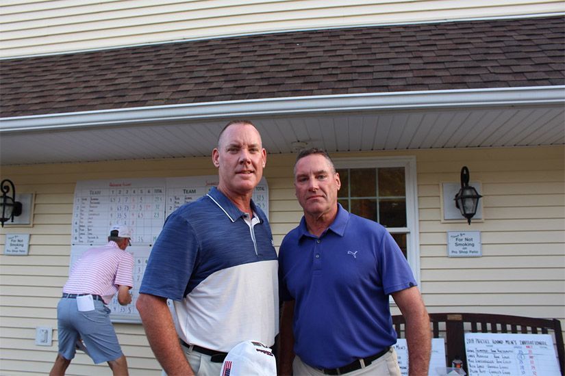 Two men are posing for a picture in front of a house