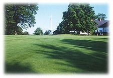A golf course with trees and a house in the background.