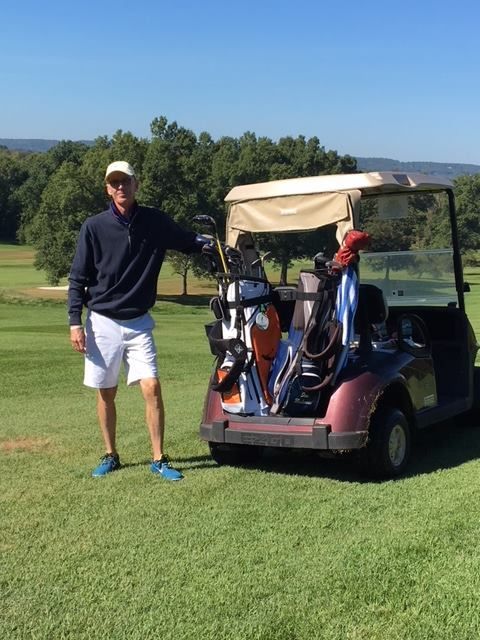A man is standing next to a golf cart on a golf course.