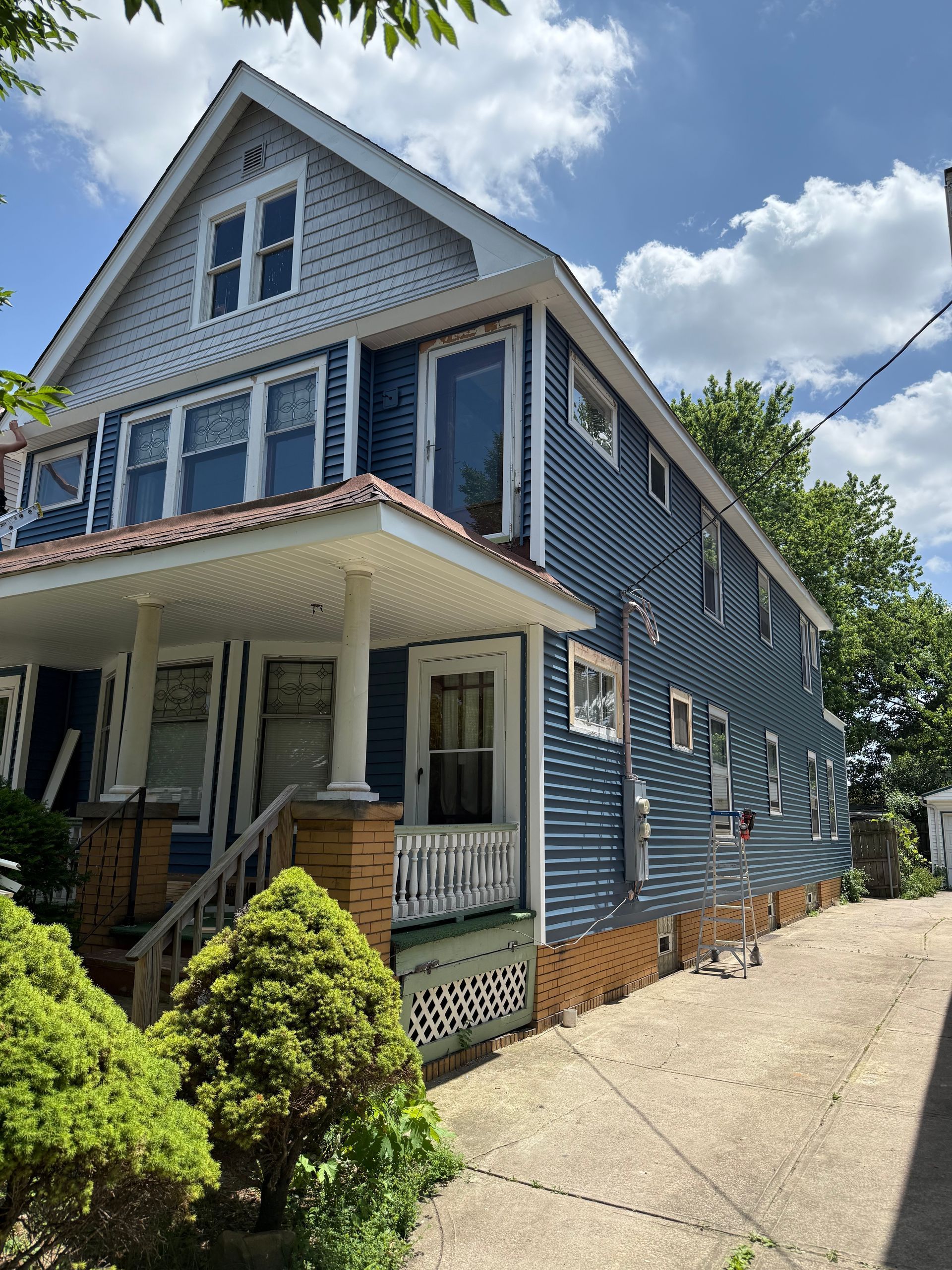 A blue and white house with a porch and a blue sky in the background.