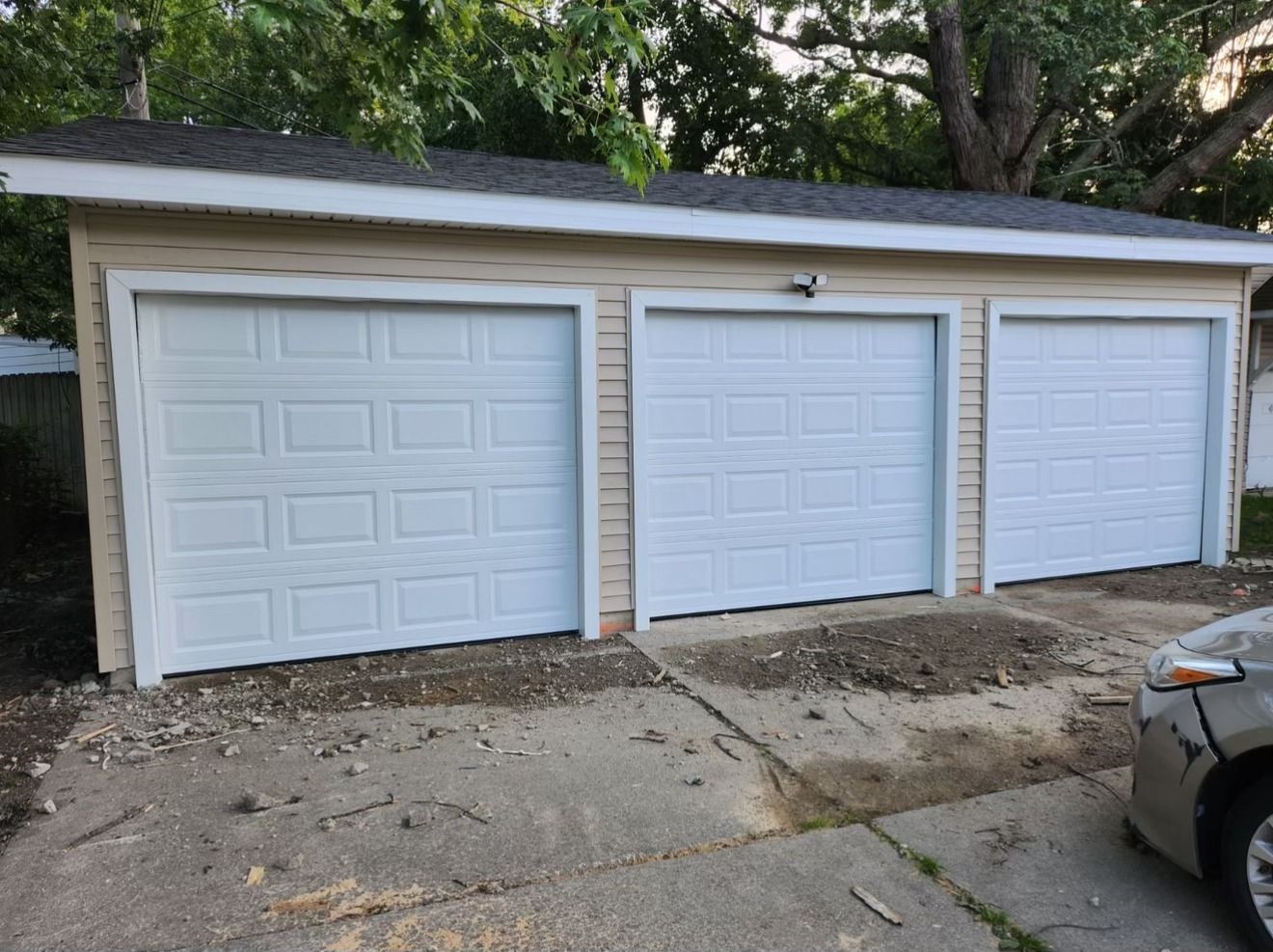 A car is parked in front of a garage with three white garage doors.