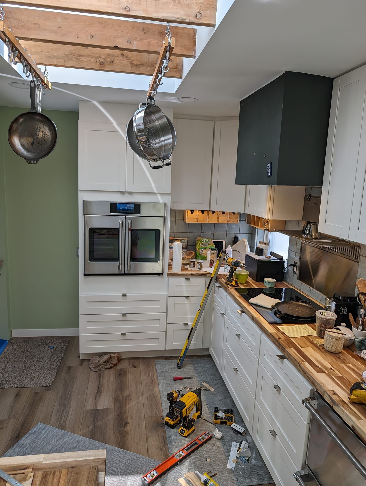Kitchen remodel in progress: white cabinets, oven, green wall, exposed beams, tools on counter and floor.