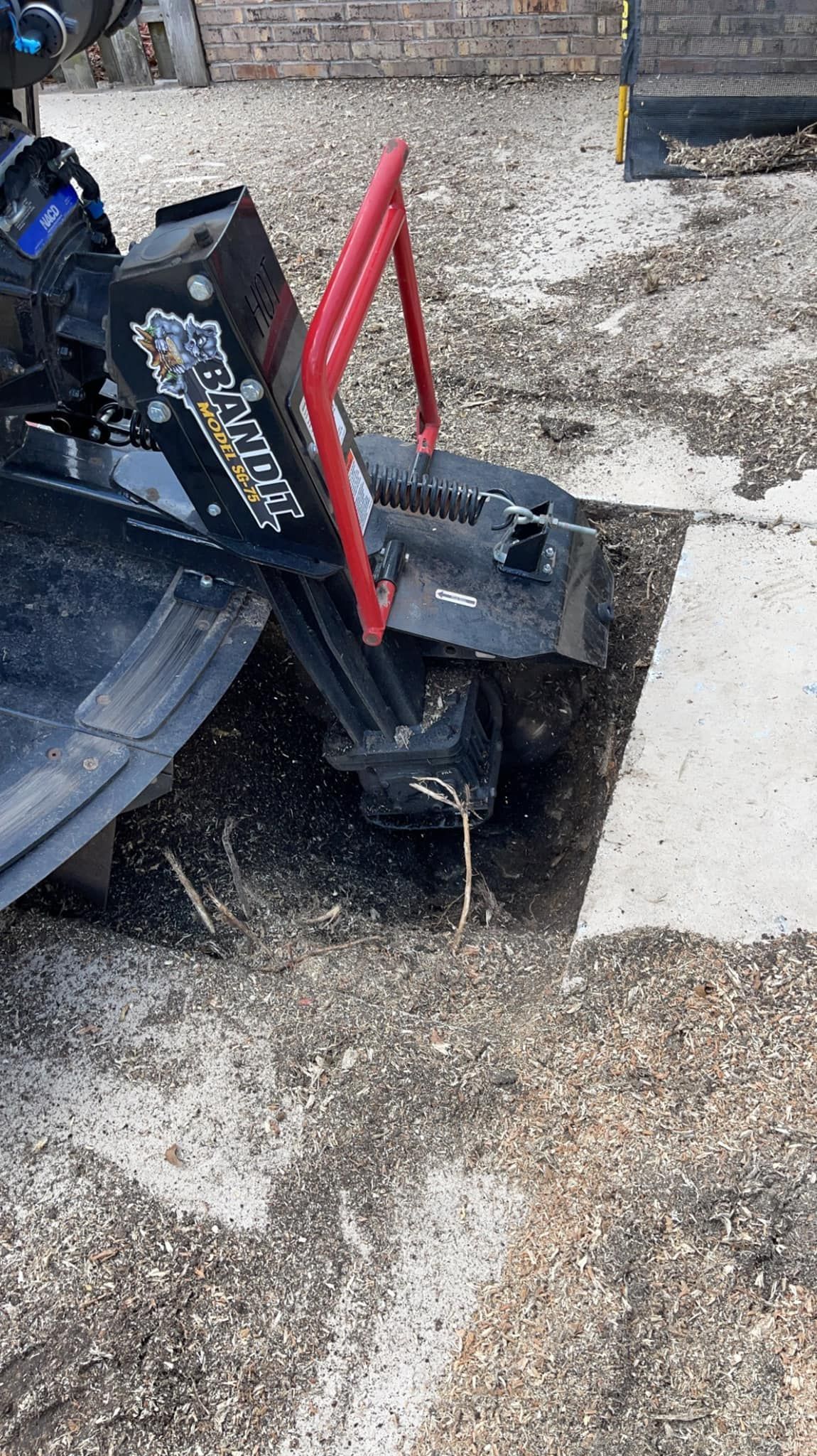 A yellow machine is cutting a tree stump in the ground.