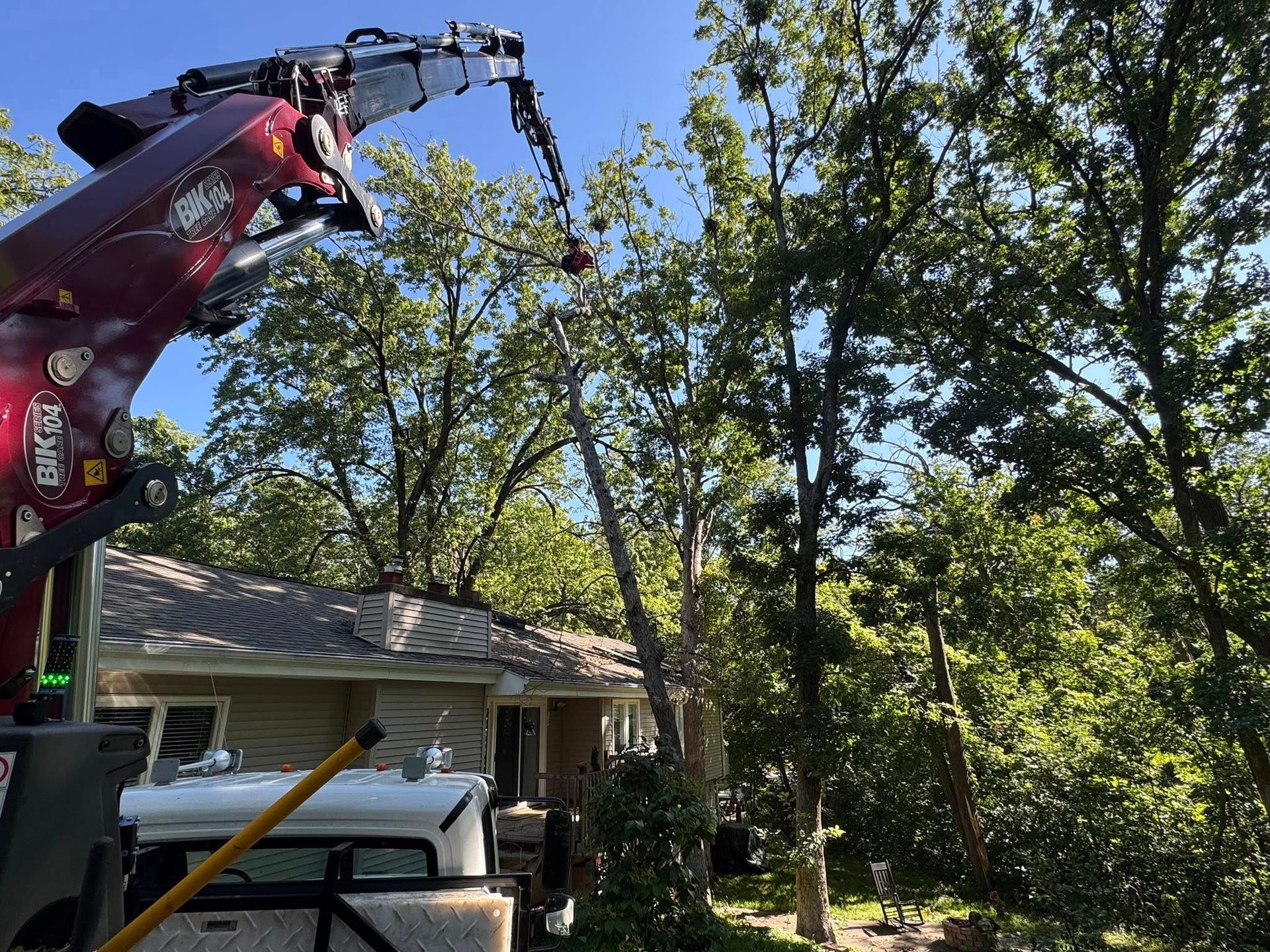 Cherry picker trimming tree branches near a house on a sunny day.