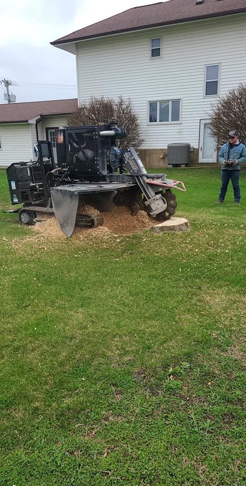 A man is standing in front of a stump grinder in a yard.