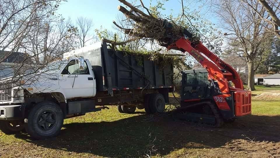 A dump truck is being loaded with branches by a forklift.