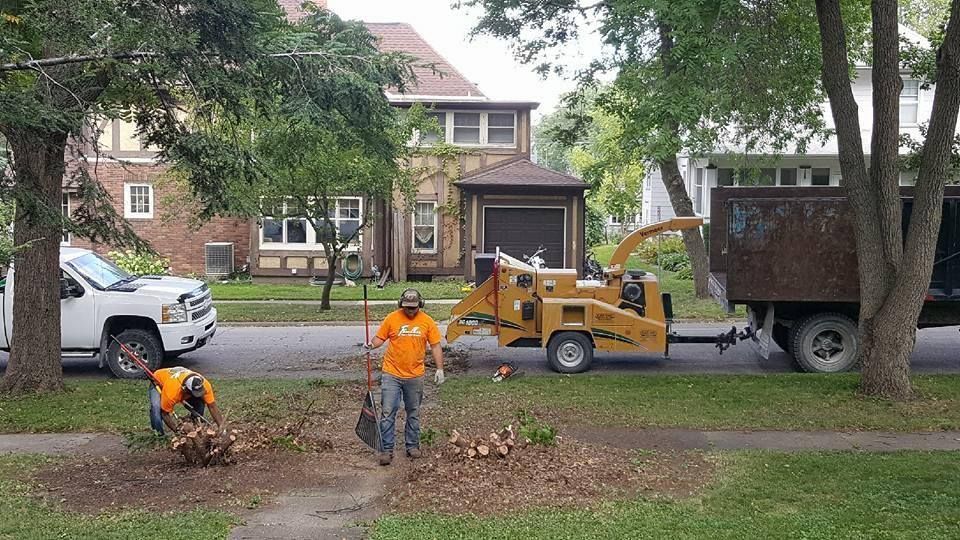 Two men are standing in front of a tree chipper in a yard.