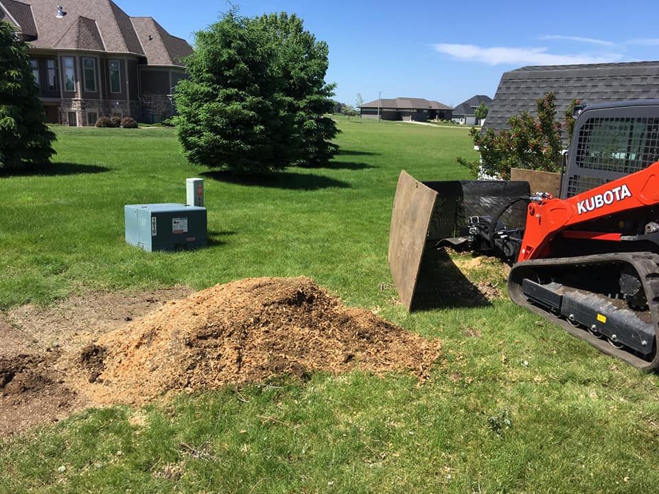 A bulldozer is cutting a tree stump in a yard.