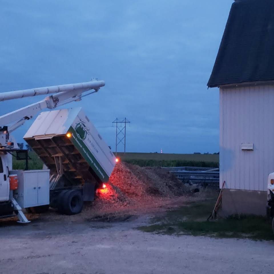 A dump truck is being loaded with dirt in front of a barn