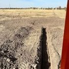 A long, narrow trench dug into dry, dirt ground in a wide-open, grassy field.