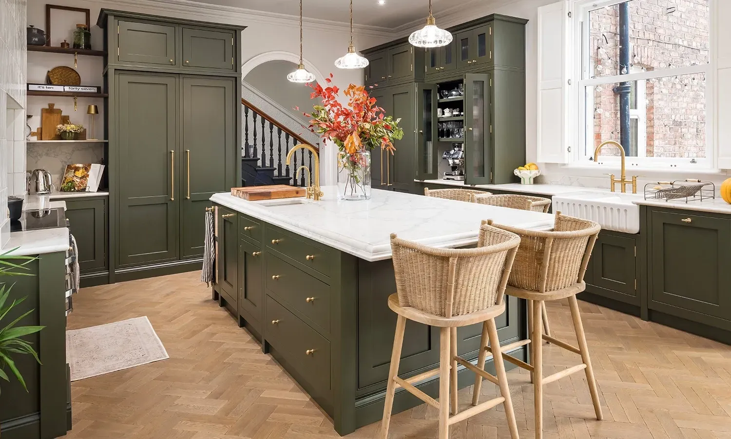 A kitchen with green cabinets , white counter tops , and wicker bar stools.