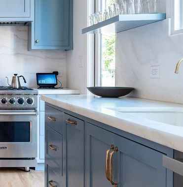 A kitchen with blue cabinets , a stove , a sink , and a window.