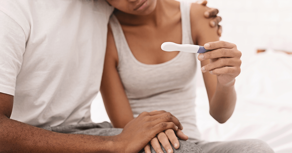 Man with arm around woman as they look at a pregnancy test.