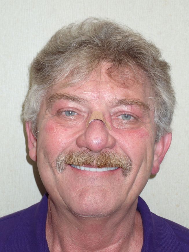 A man with a mustache is smiling and wearing a purple shirt.