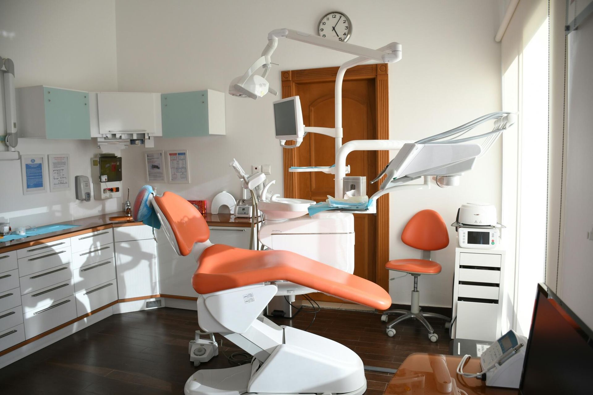 A dental office with an orange dental chair and a clock on the wall.