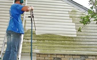 Man pressure washing a brick wall outdoors.