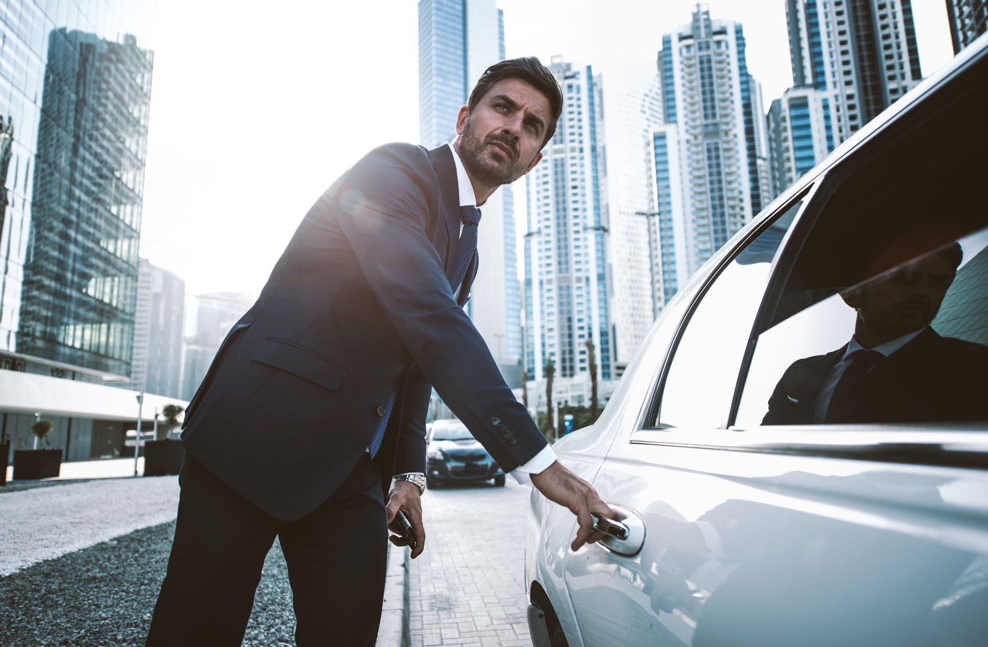 A man in a suit is opening the door of a limousine.