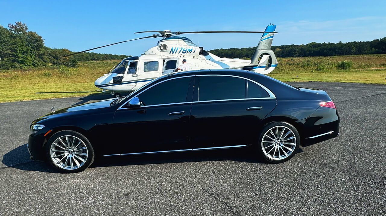A black car is parked in front of a helicopter.