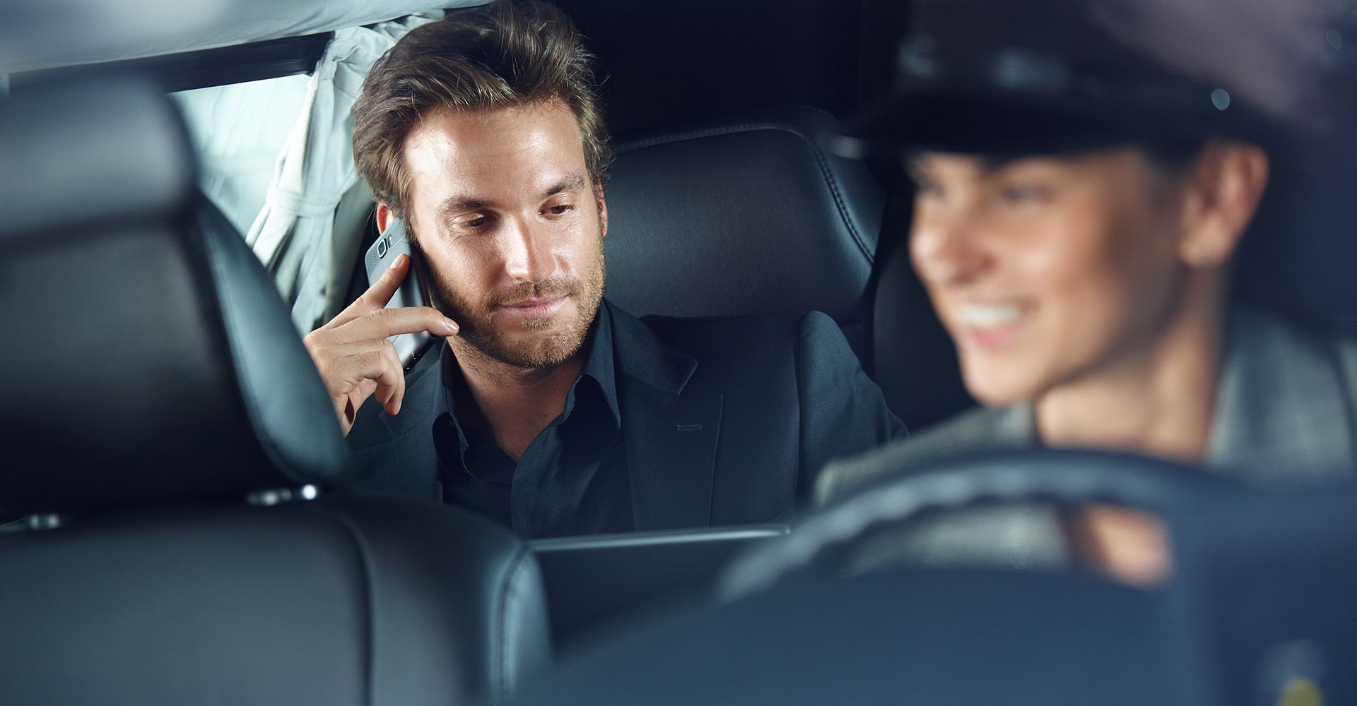 A man is sitting in the back seat of a car talking on a cell phone.