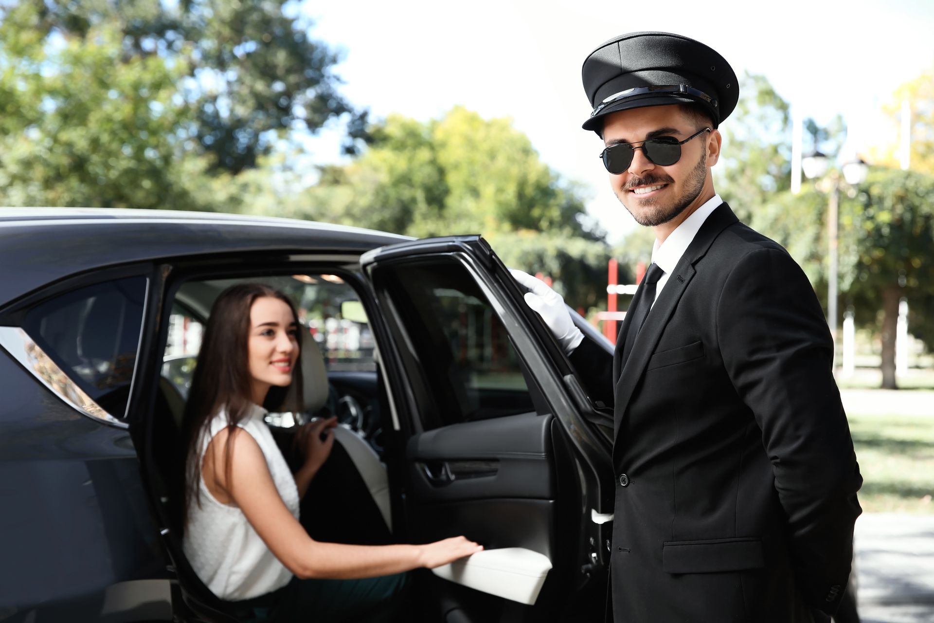 A chauffeur is opening the door of a limousine for a woman.