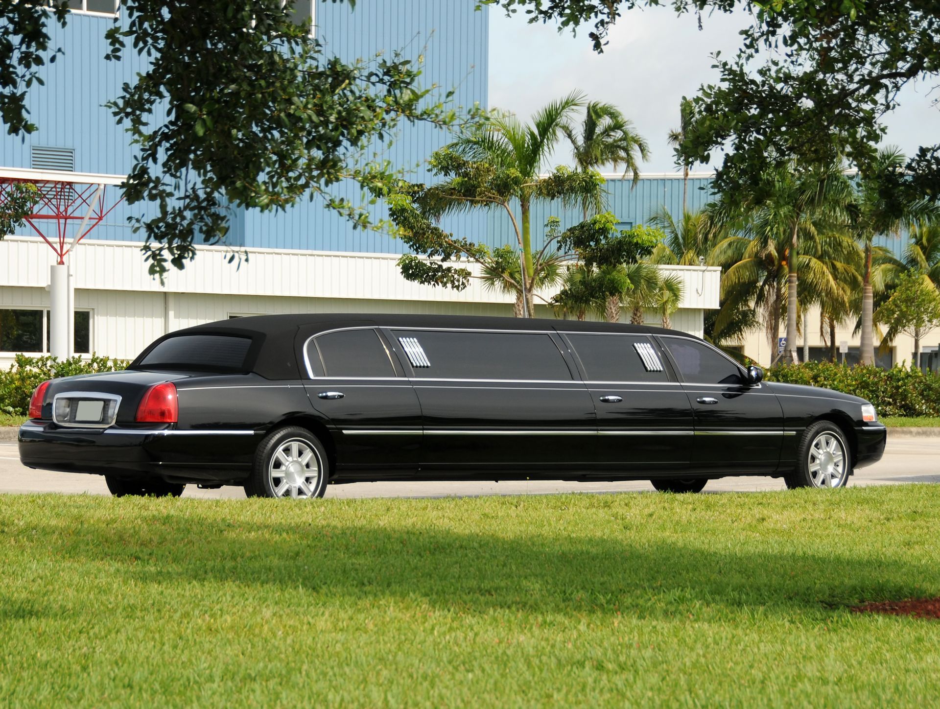 A black limousine is parked in the grass in front of a building.