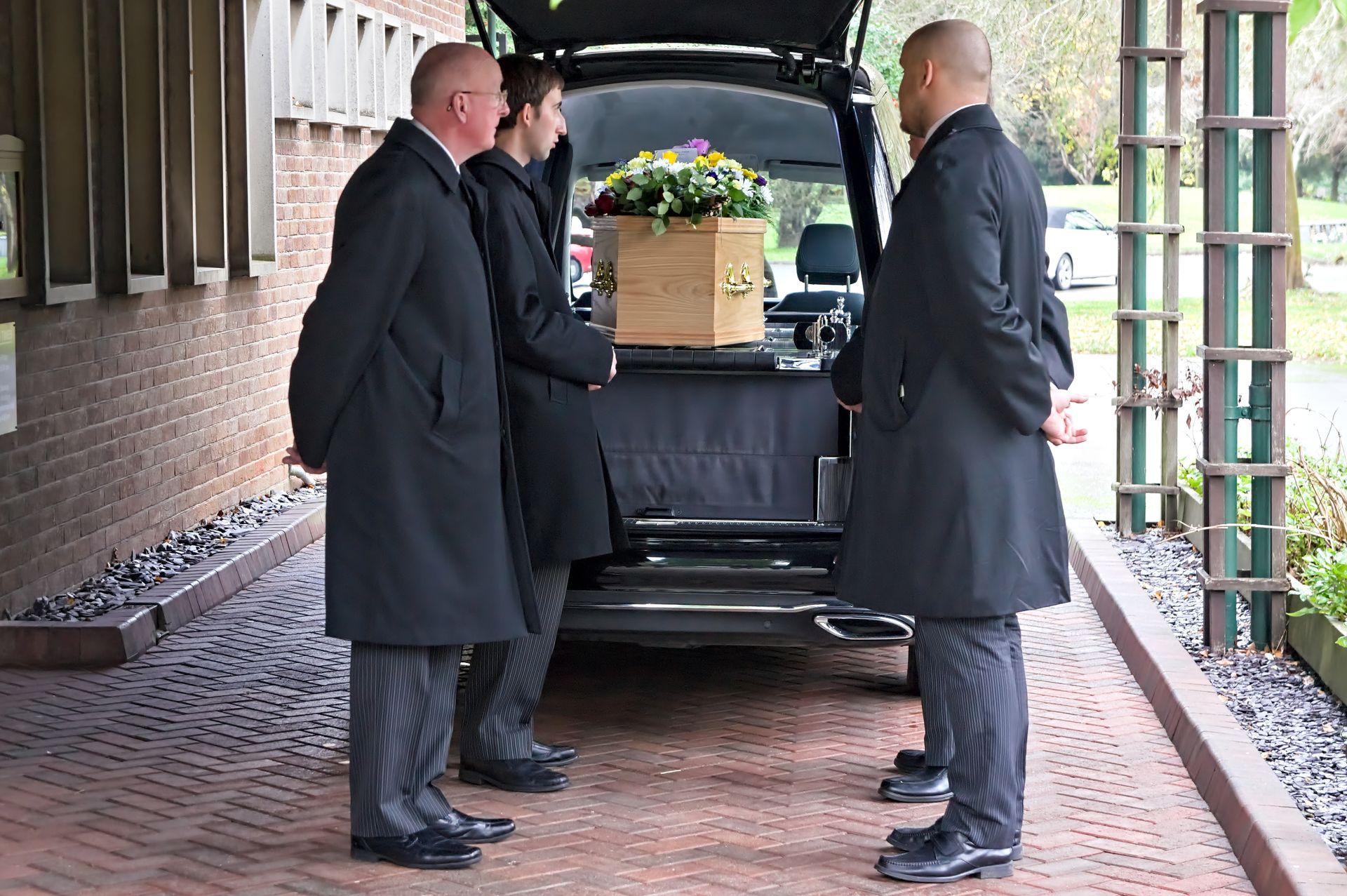 Three men in black coats are standing next to a coffin