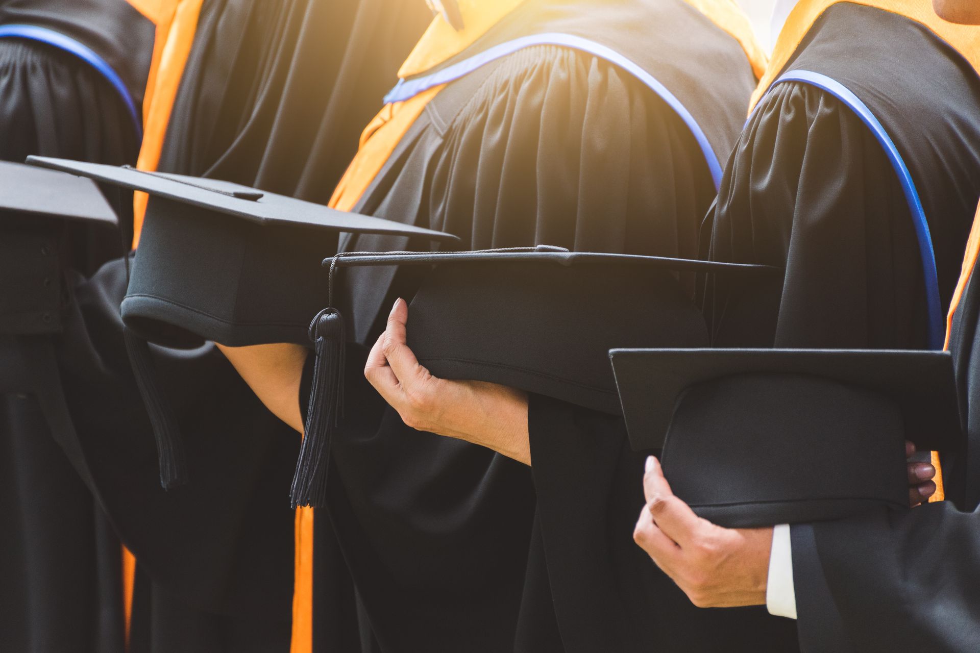 A group of graduates are standing in a row holding their caps and gowns.