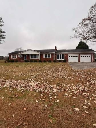 Brick ranch home with three-car garage on a lawn covered in fallen leaves under an overcast sky.