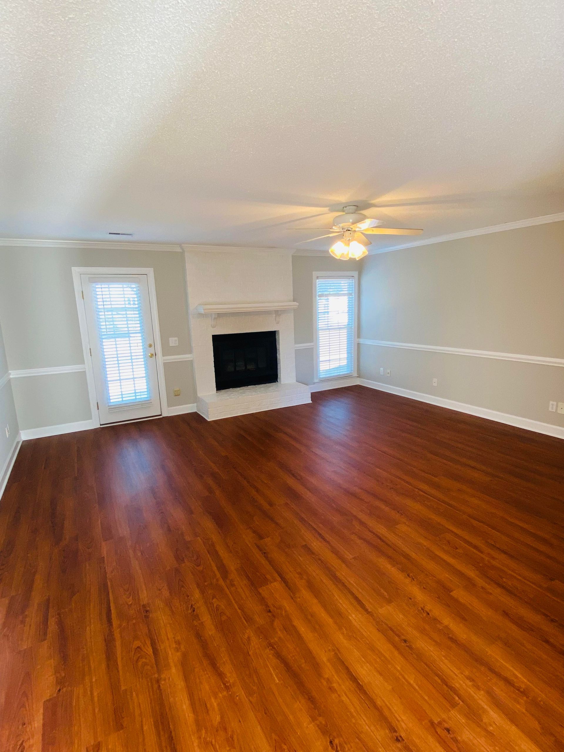 Empty beige bedroom with wood floors, ceiling light, and a window with blinds