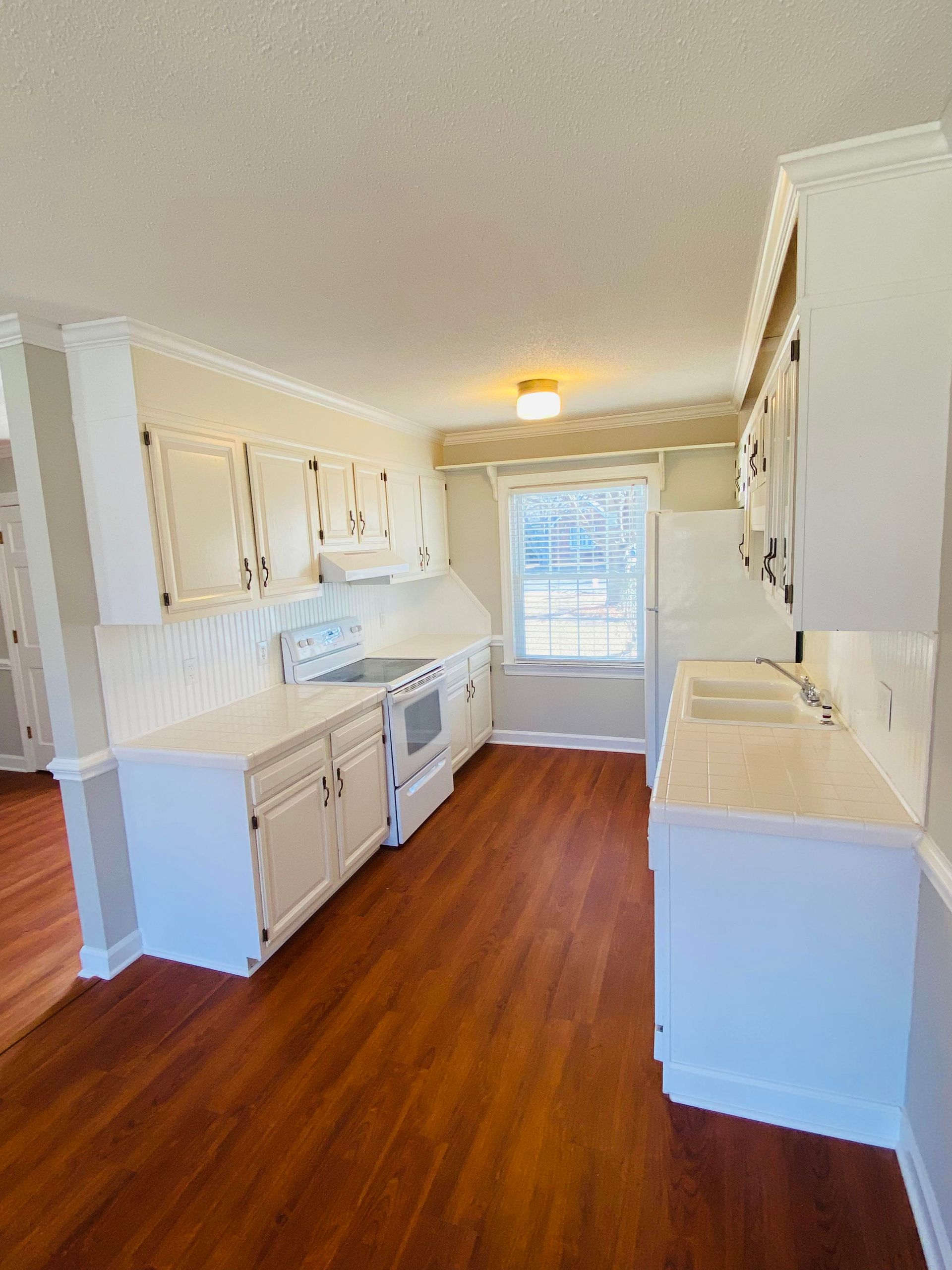 Empty beige room with wood flooring, two windows, and a ceiling fan with light