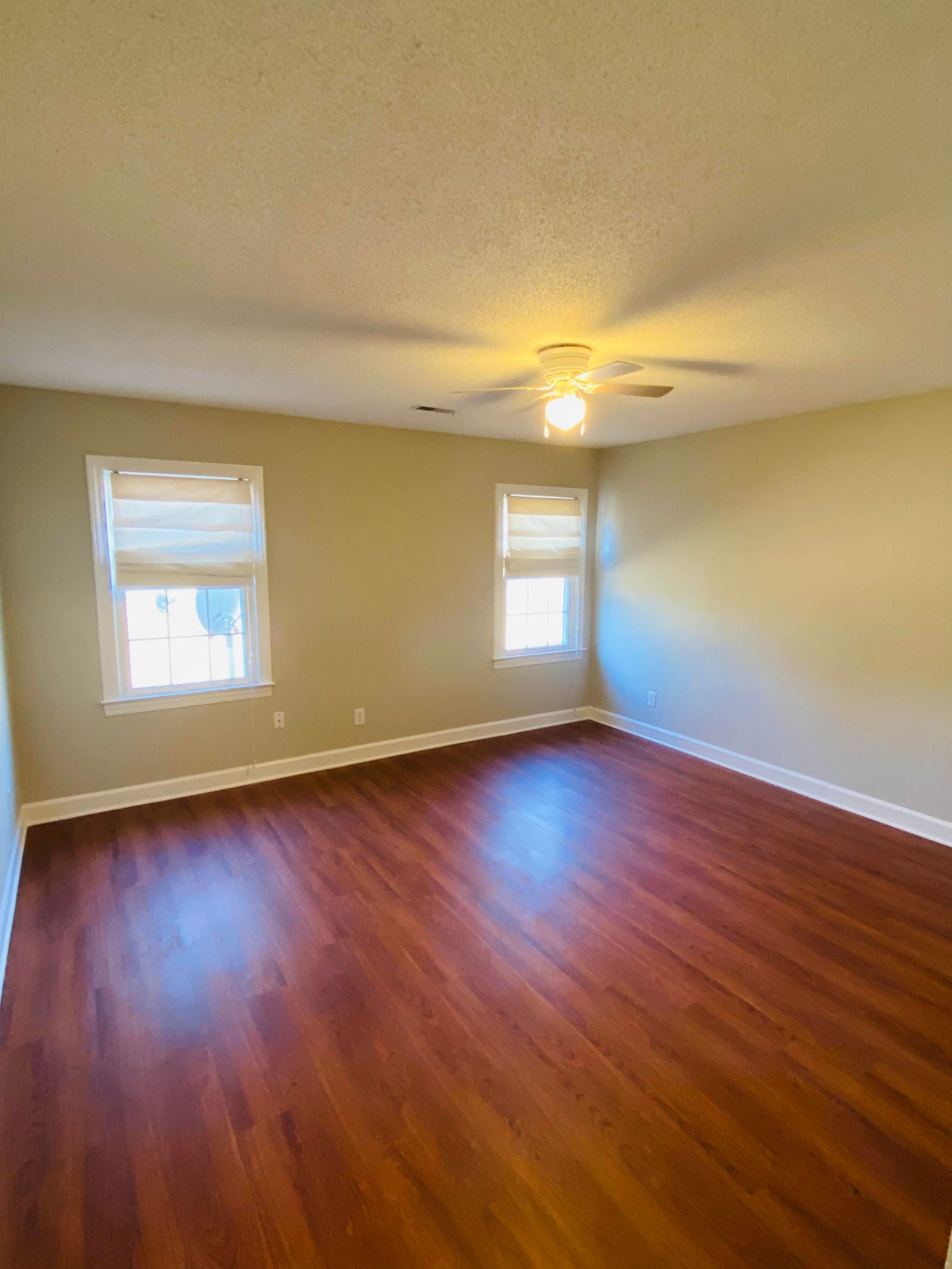 Empty living room with hardwood floors, fireplace, and large windows with blinds