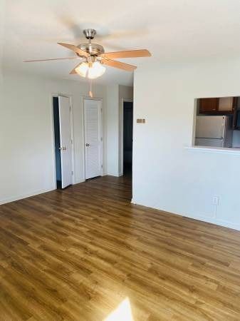 Empty living room with wood-look flooring, white walls, closet doors, and a ceiling fan.