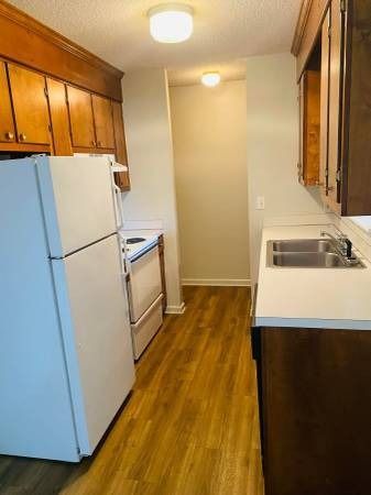 Kitchen with white appliances, wooden cabinets, and a long hallway.