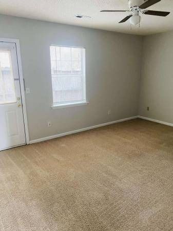 Empty room with beige carpet, window, white door, and ceiling fan. Gray walls.