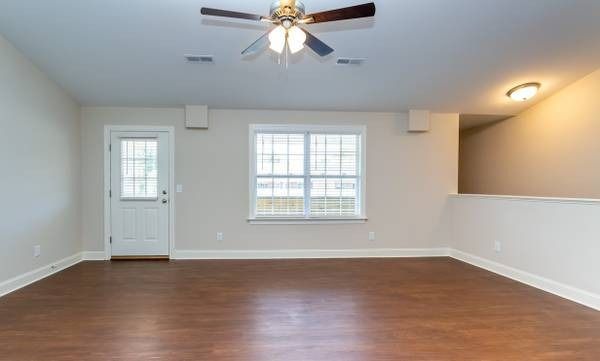 Empty living room with wood flooring, white walls, door, window, and ceiling fan.