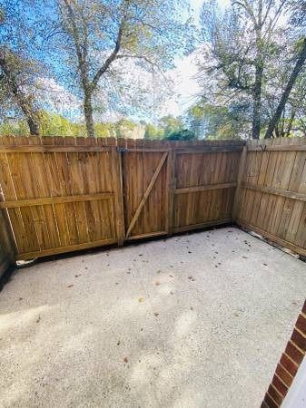 Wooden fenced-in backyard with gravel ground, gate, and trees in the background.