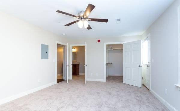 Spacious, carpeted bedroom with white walls, three doorways (bathroom, closet, exit), and a ceiling fan.