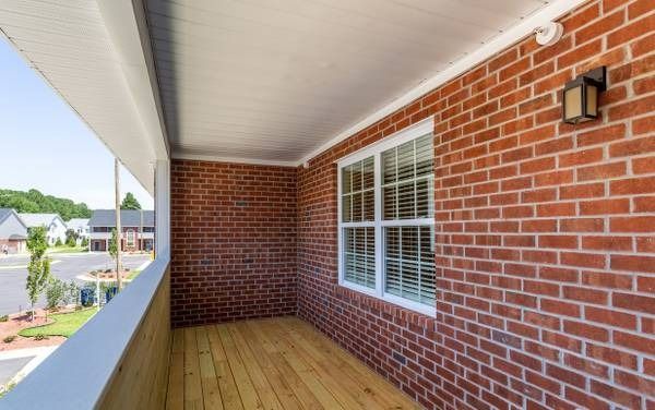 Small balcony with red brick walls, white trim, and wooden floor; houses in the background.