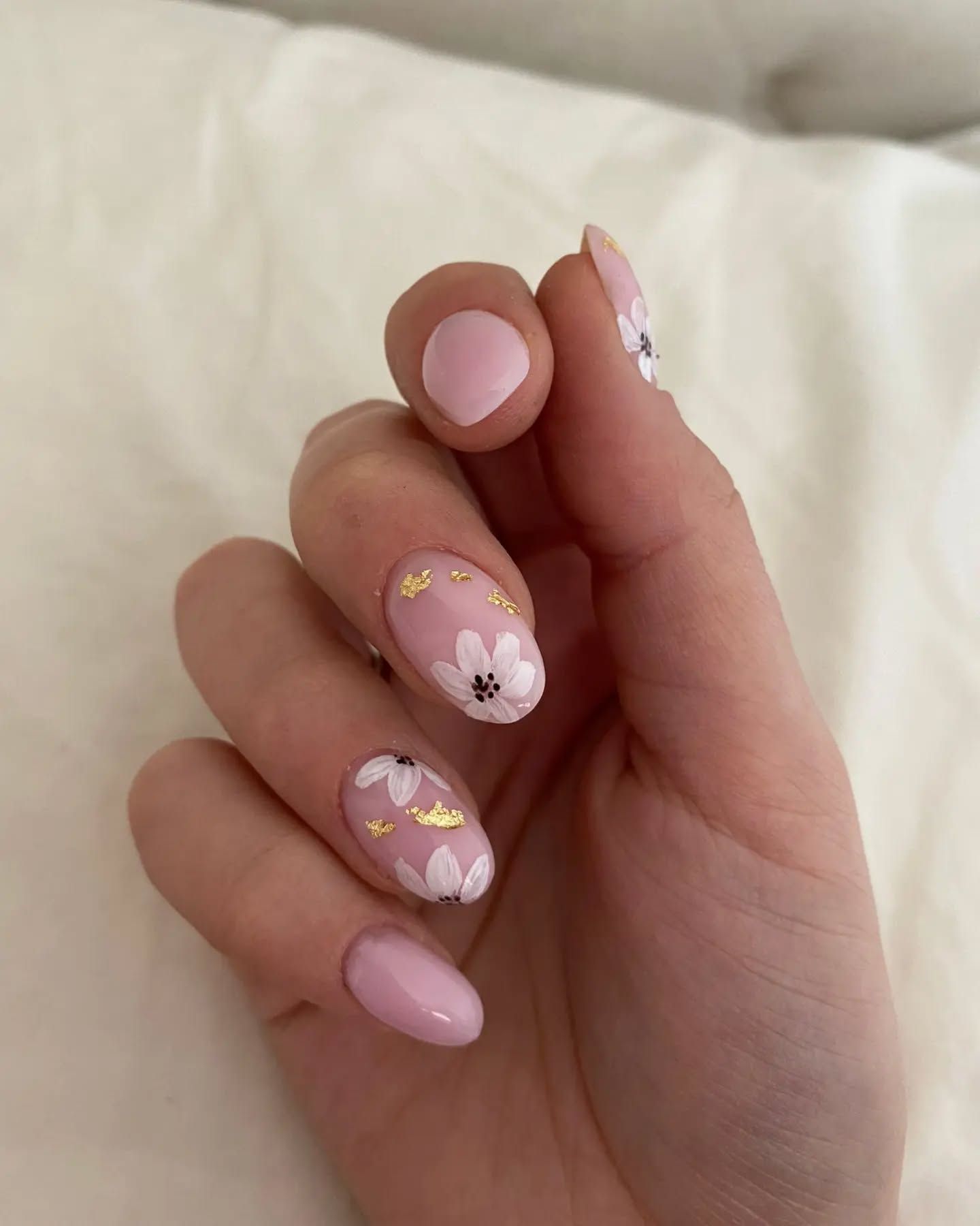 La mano di una donna con le unghie rosa e fiori bianchi.