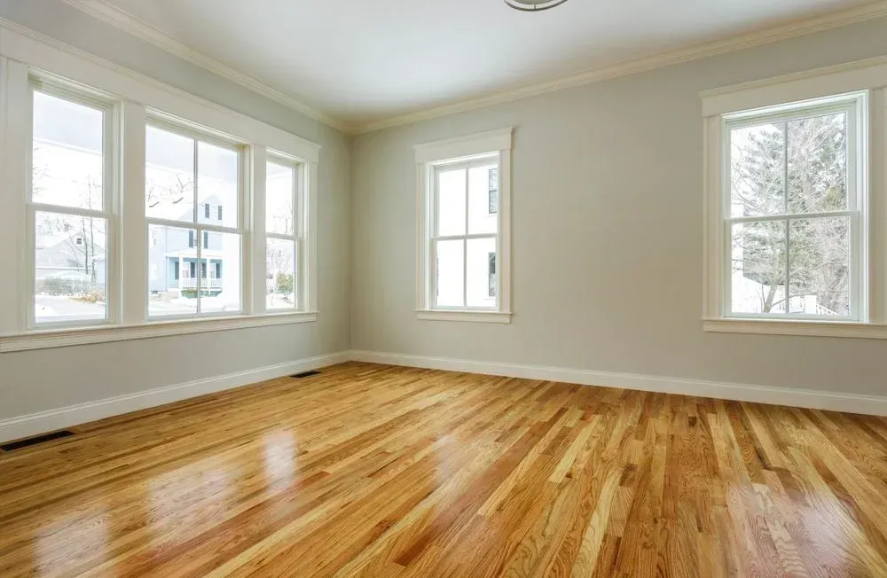 An empty room with hardwood floors and lots of windows.