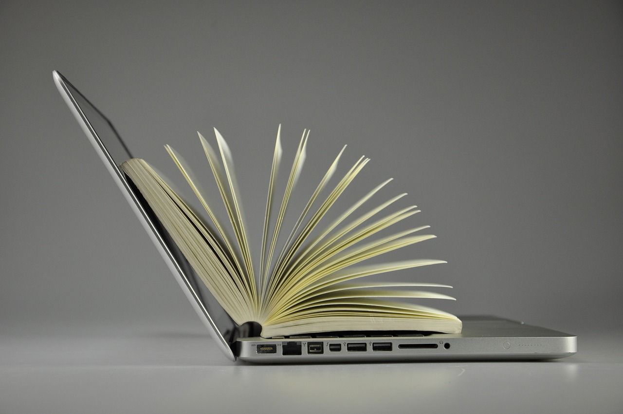 Image of a laptop with an open book fanning out on top between the screen and the keyboard.