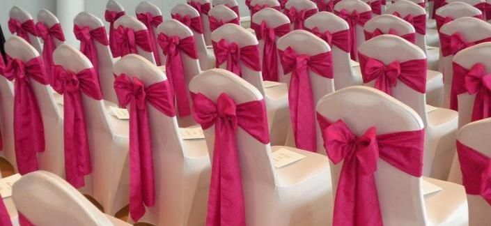 Rows of white chairs with bright pink bows decorated for an event