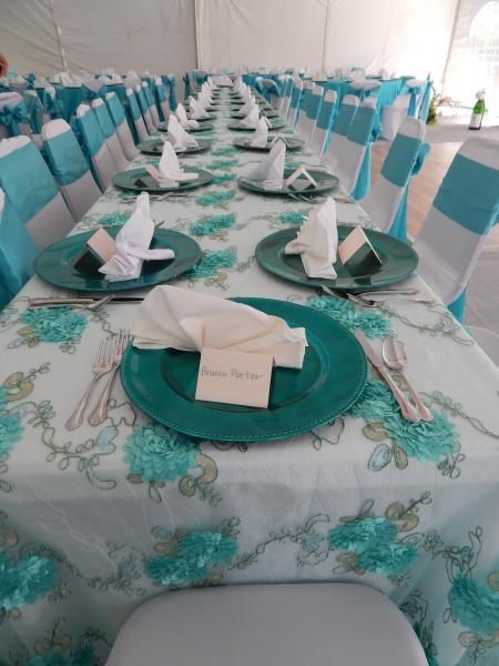 Decorated banquet table with turquoise plates, white napkins, and teal chair covers in a bright tent