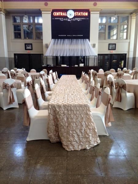 Banquet hall with long draped tables and white-covered chairs facing a stage and Central Station sign