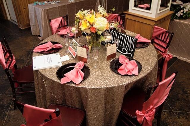 Decorated round table with pink favors, flowers, and a sign at a formal event