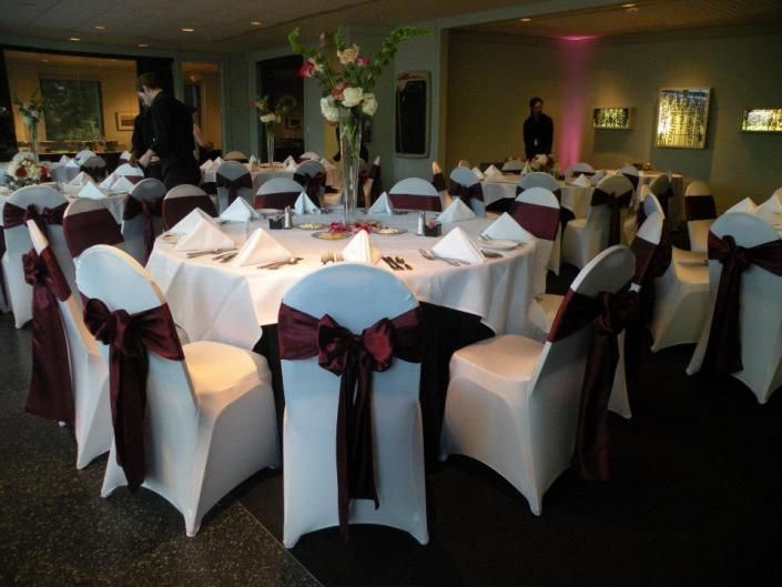 Round banquet tables in a decorated reception hall with white chair covers and burgundy bows.
