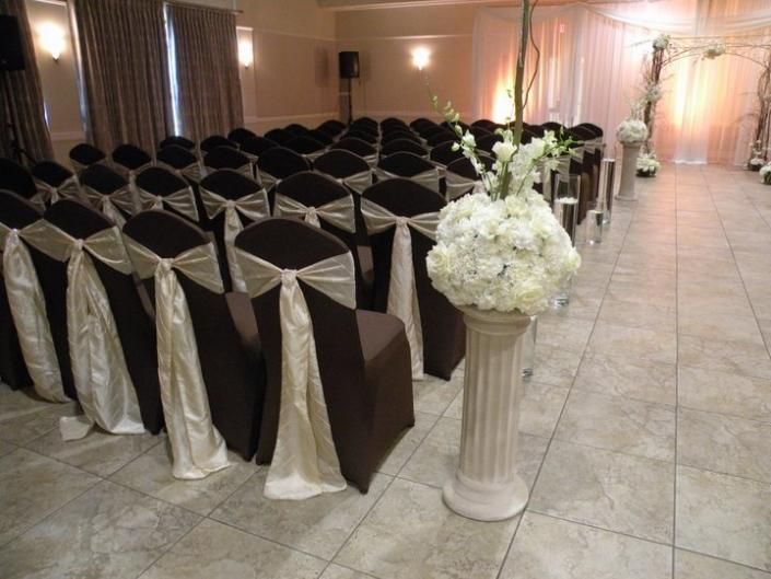 Elegant banquet hall with rows of black chairs in white covers and a white floral arrangement on a pedestal