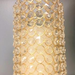 Close-up of a gold beaded cylindrical lamp or vase with circular crystal-like accents.