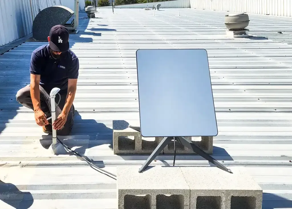 Two men installing a speaker on a white wall near a TV. One man is holding the speaker.