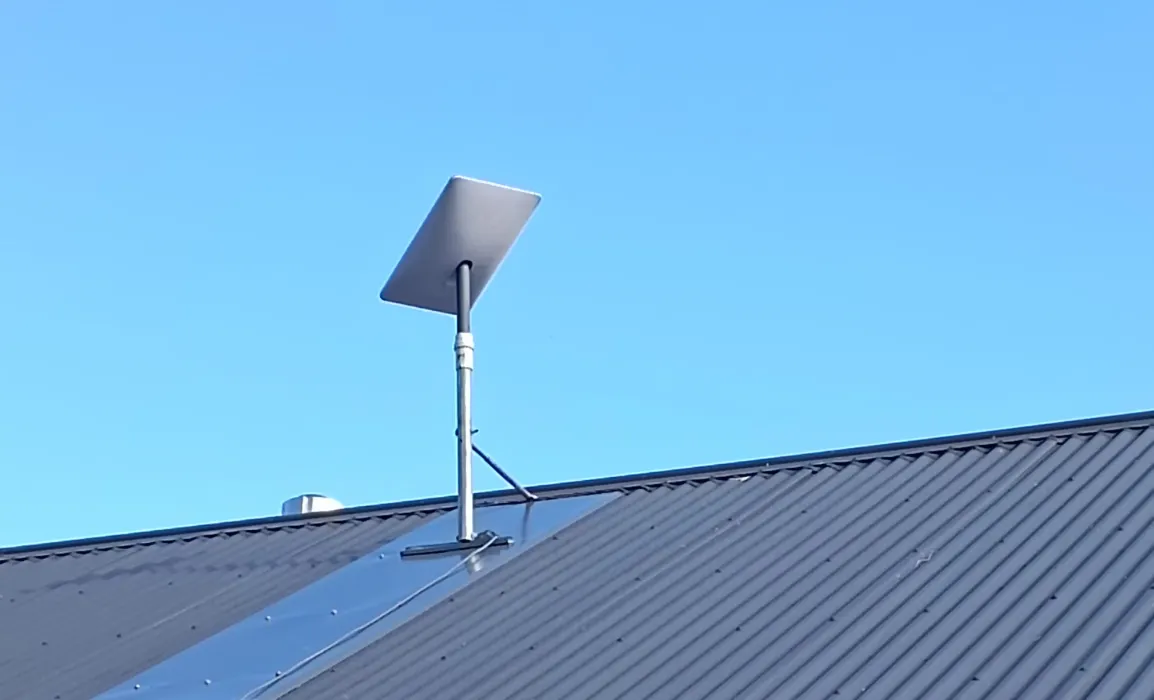 Starlink satellite dish mounted on a rooftop, angled towards the clear blue sky.